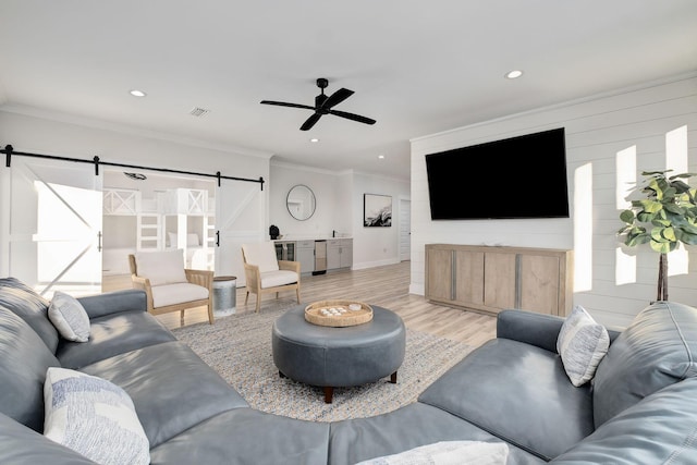 living area with a barn door, ceiling fan, ornamental molding, light wood-style floors, and recessed lighting