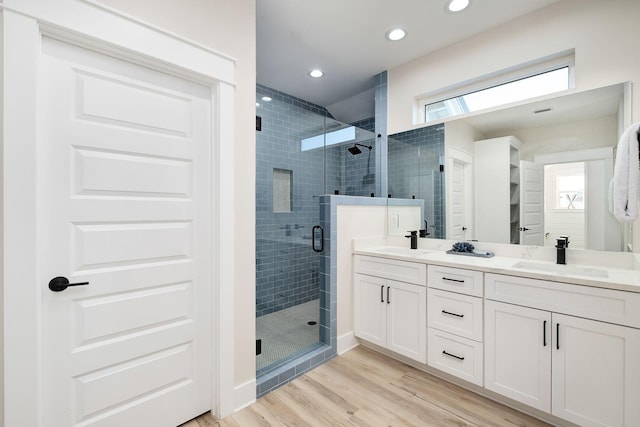 bathroom featuring a shower stall, wood finished floors, double vanity, and recessed lighting