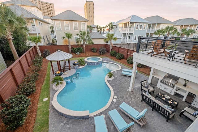 pool at dusk featuring a residential view, a fenced backyard, area for grilling, a gazebo, and a pool with connected hot tub