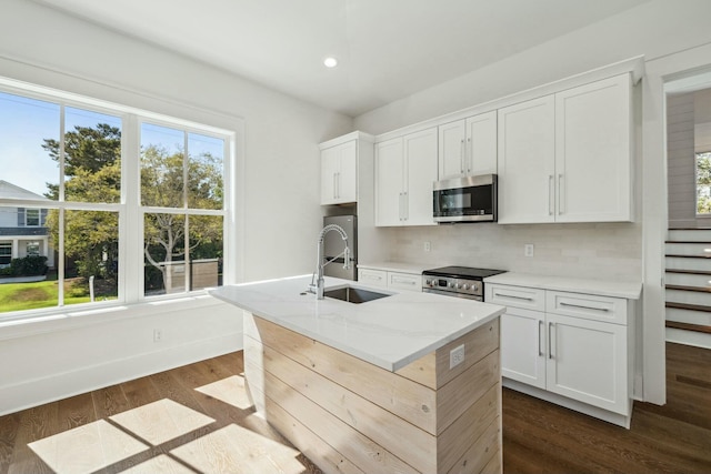 kitchen featuring a sink, stainless steel appliances, dark wood-type flooring, a center island with sink, and backsplash