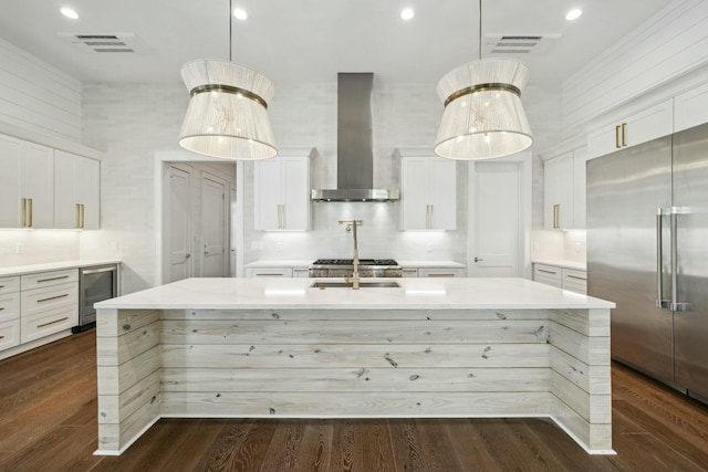 kitchen with wine cooler, stainless steel built in fridge, visible vents, wall chimney exhaust hood, and a center island with sink