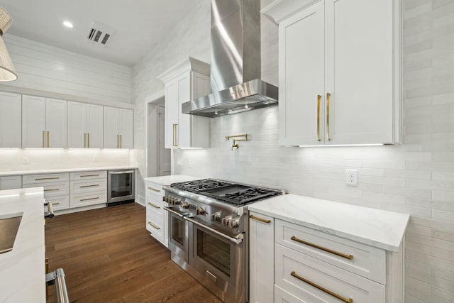 kitchen featuring white cabinetry, wall chimney range hood, range with two ovens, visible vents, and wine cooler