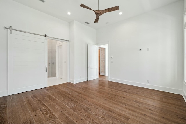 unfurnished bedroom featuring recessed lighting, wood finished floors, a barn door, baseboards, and a ceiling fan