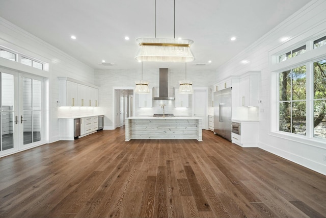 kitchen featuring wall chimney range hood, crown molding, built in fridge, light countertops, and french doors
