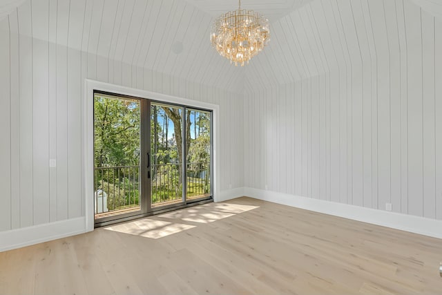 unfurnished dining area featuring light wood-type flooring, a notable chandelier, wood walls, and baseboards