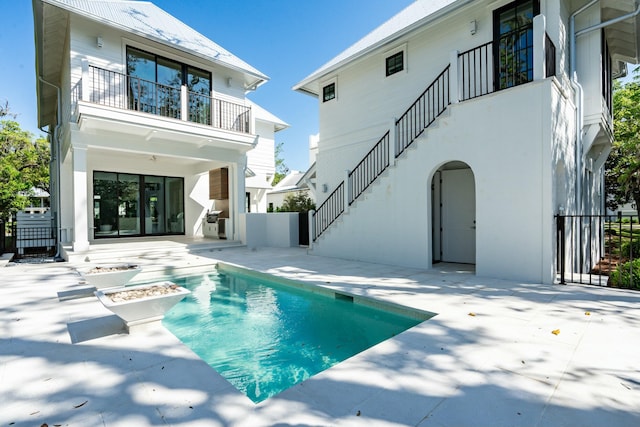 rear view of house with a balcony, a fenced in pool, a patio area, fence, and stairway