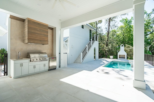view of pool with a sink, a patio area, exterior kitchen, an outdoor fireplace, and area for grilling