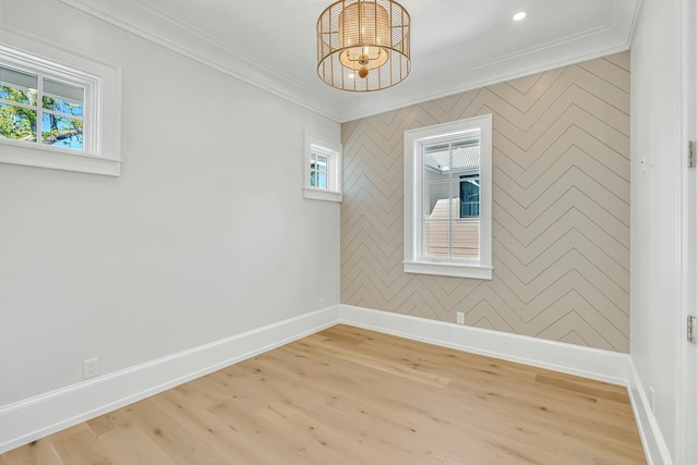 spare room featuring crown molding, light wood-style flooring, a chandelier, and baseboards