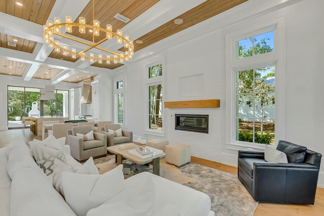 living area with a chandelier, wooden ceiling, beam ceiling, a glass covered fireplace, and light wood finished floors
