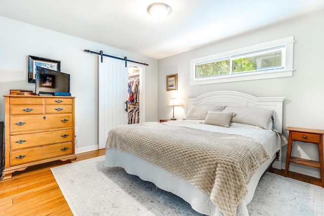 bedroom featuring a closet, a spacious closet, a barn door, and light wood-style floors