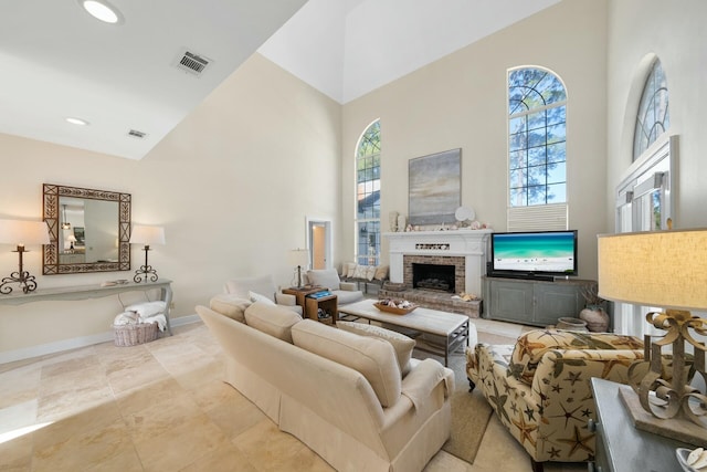 living area featuring baseboards, visible vents, a brick fireplace, and a towering ceiling