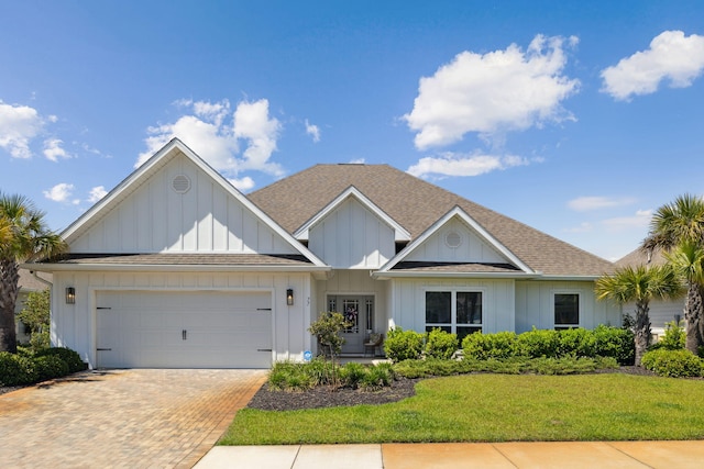 view of front of property with a front yard, decorative driveway, roof with shingles, board and batten siding, and an attached garage