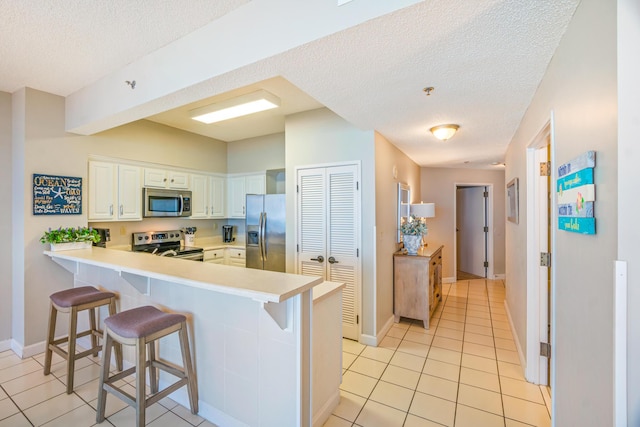kitchen with a kitchen breakfast bar, a textured ceiling, appliances with stainless steel finishes, light tile patterned floors, and a peninsula