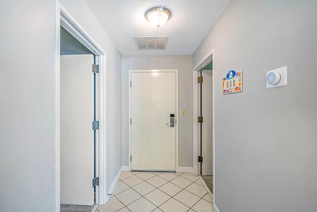 doorway with baseboards, a textured ceiling, visible vents, and light tile patterned floors