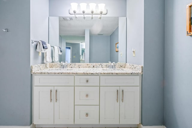 full bathroom featuring double vanity, a textured ceiling, visible vents, and a sink