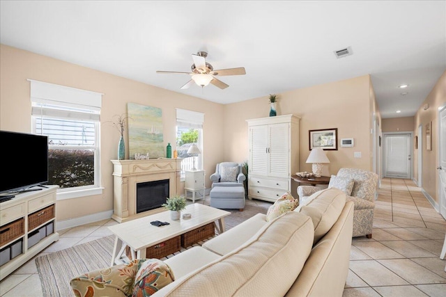 living area with ceiling fan, a glass covered fireplace, baseboards, light tile patterned floors, and visible vents