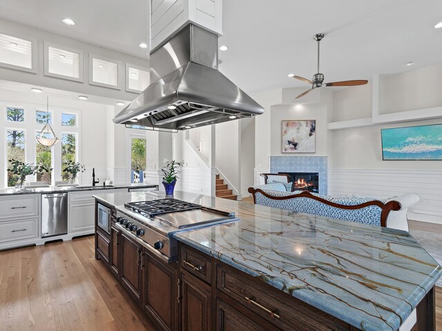 182 My Way, Santa Rosa Beach, FL 32459 - kitchen featuring stainless steel gas cooktop, a fireplace, island range hood, light wood-type flooring, and a ceiling fan
