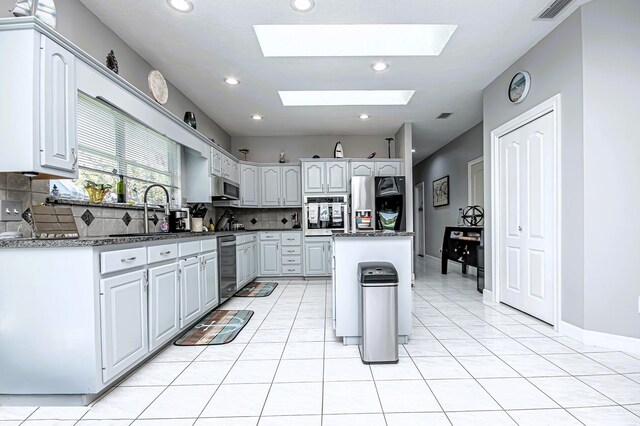 kitchen with tasteful backsplash, a skylight, appliances with stainless steel finishes, a kitchen island, and a sink