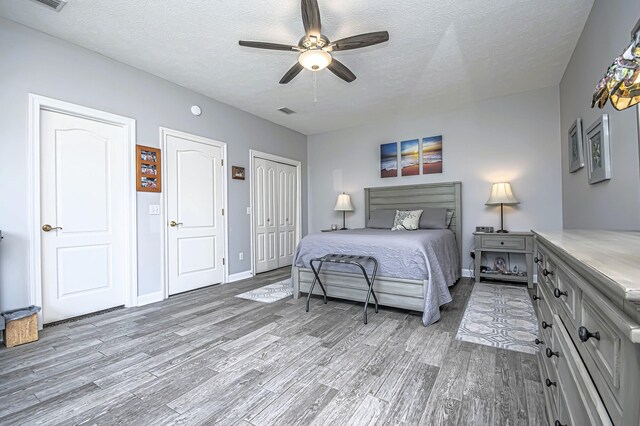 bedroom with a textured ceiling, two closets, light wood-type flooring, and baseboards