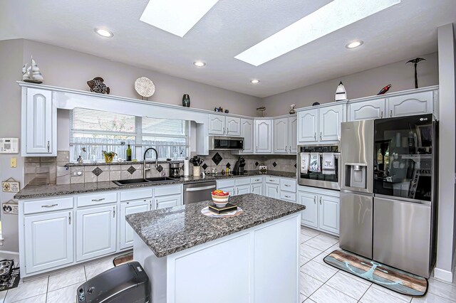 kitchen with dark stone counters, a sink, decorative backsplash, a skylight, and appliances with stainless steel finishes