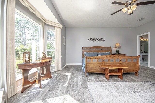 bedroom featuring wood finished floors, ensuite bath, baseboards, visible vents, and a textured ceiling