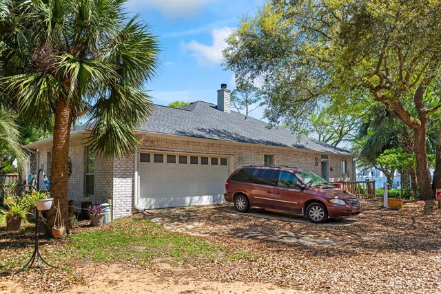 view of side of home with a chimney, brick siding, a shingled roof, a garage, and driveway