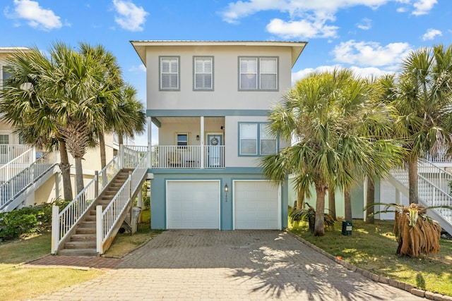 raised beach house featuring stucco siding, decorative driveway, stairway, and a garage