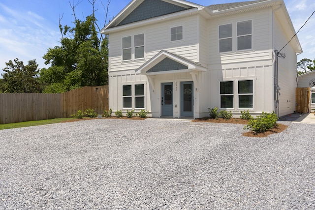 view of front of home featuring board and batten siding, fence, and gravel driveway