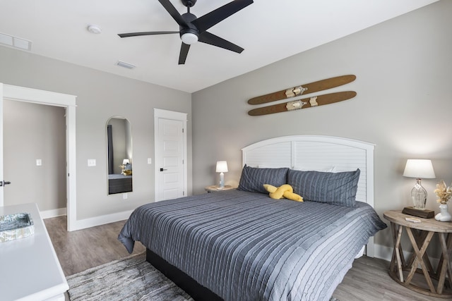 bedroom featuring visible vents, a ceiling fan, wood finished floors, baseboards, and arched walkways