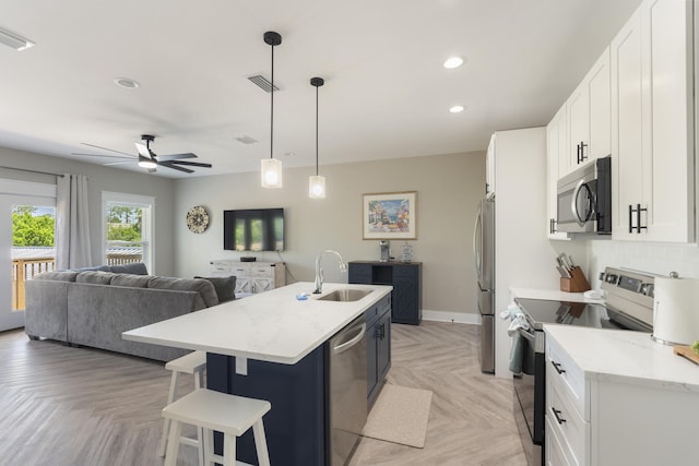 kitchen featuring appliances with stainless steel finishes, a sink, open floor plan, visible vents, and a center island with sink