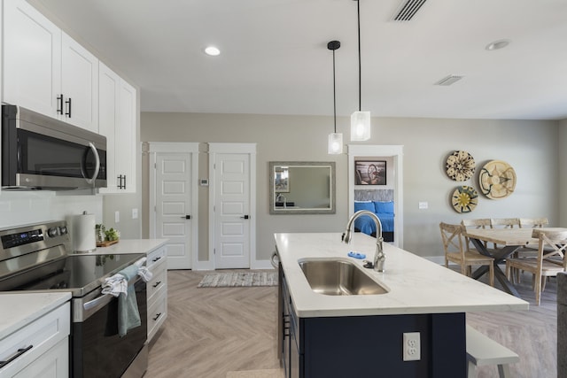 kitchen featuring a sink, an island with sink, stainless steel appliances, white cabinetry, and visible vents