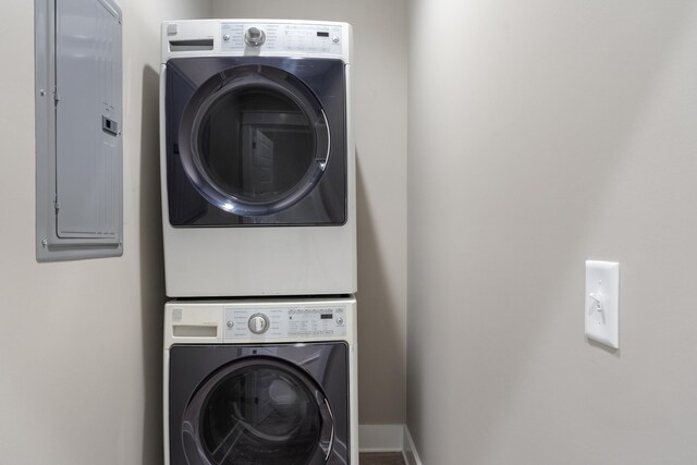 laundry room featuring baseboards, laundry area, stacked washer / dryer, and electric panel