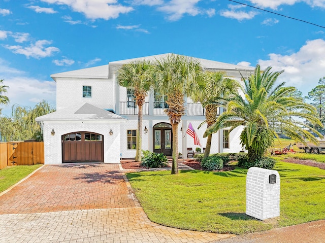 view of front of home with decorative driveway, a front lawn, a balcony, and french doors
