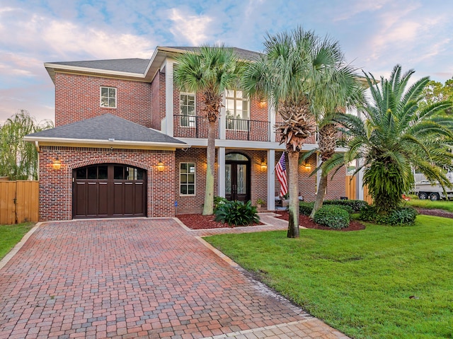view of front of house featuring french doors, brick siding, decorative driveway, a front lawn, and an attached garage