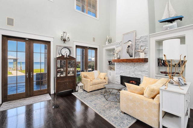 living room with french doors, a towering ceiling, a fireplace, wood finished floors, and built in shelves