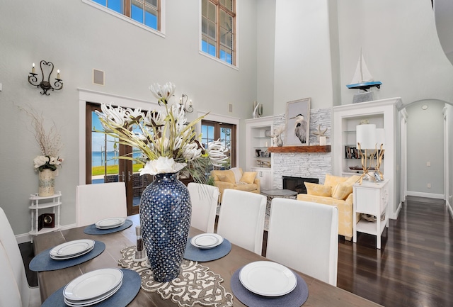 dining space with visible vents, baseboards, a stone fireplace, a high ceiling, and dark wood-type flooring