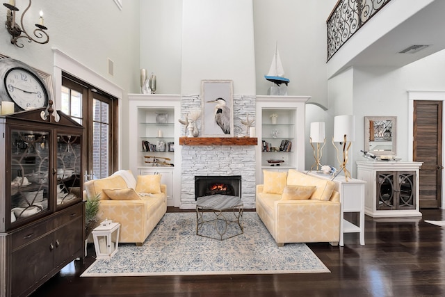 living room with a towering ceiling, wood finished floors, a stone fireplace, and visible vents