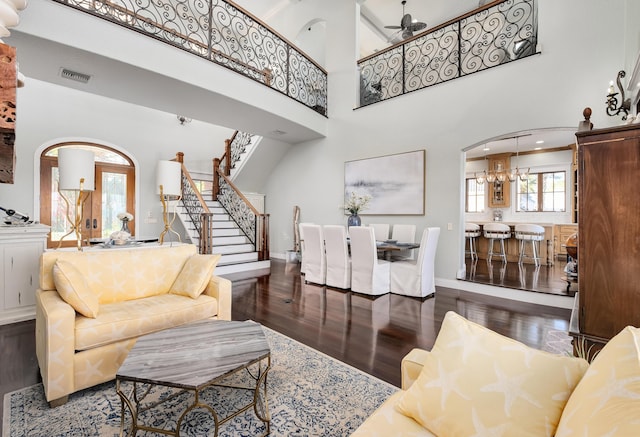 living room with a high ceiling, arched walkways, wood finished floors, visible vents, and stairway