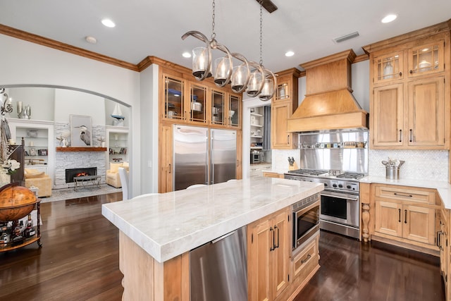 kitchen with a center island, premium range hood, a notable chandelier, built in appliances, and ornamental molding