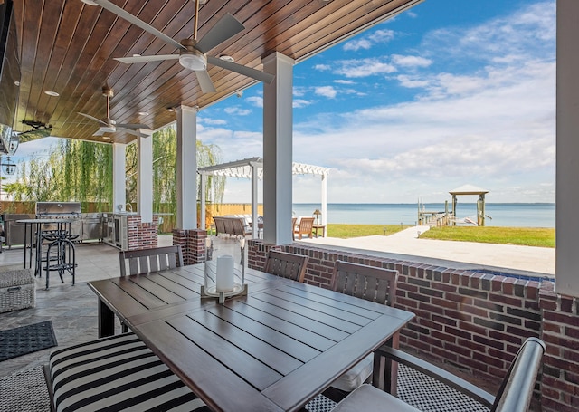 view of patio with an outdoor kitchen, outdoor dining area, ceiling fan, and a water view