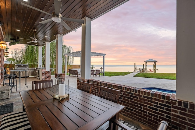 patio terrace at dusk with exterior kitchen, ceiling fan, a water view, and outdoor dining space