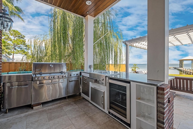 view of patio with exterior kitchen, a sink, wine cooler, a water view, and a grill