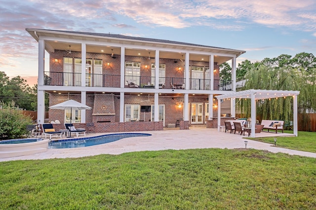 back of property at dusk featuring a yard, a patio area, brick siding, and a balcony