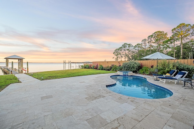 pool at dusk with a water view, a pool with connected hot tub, a fenced backyard, and a patio area