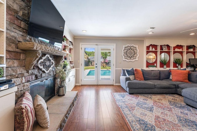 living room featuring french doors, a stone fireplace, crown molding, baseboards, and hardwood / wood-style floors