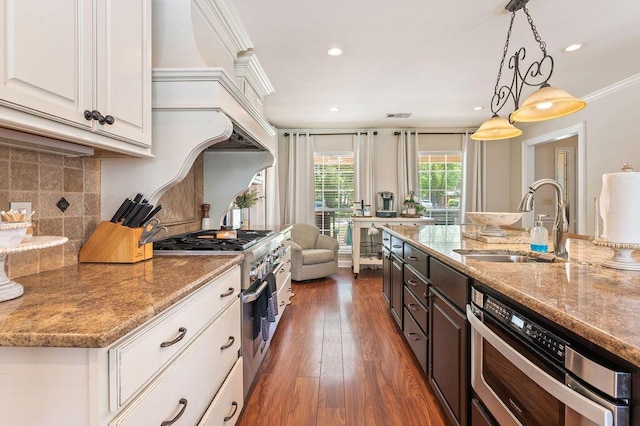 kitchen with decorative backsplash, light stone countertops, stainless steel stove, a sink, and white cabinets