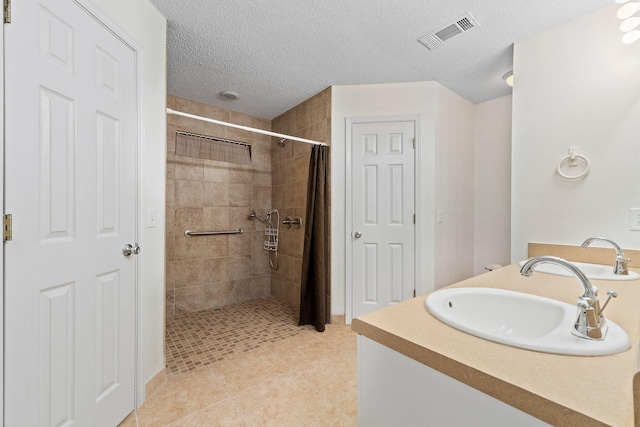 full bathroom with tile patterned floors, visible vents, tiled shower, and a sink
