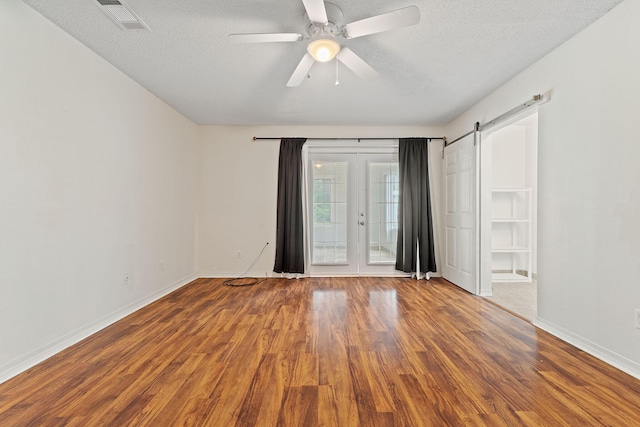 empty room featuring a ceiling fan, visible vents, baseboards, a textured ceiling, and wood finished floors