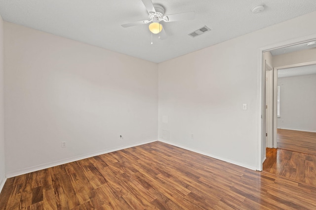 spare room with ceiling fan, visible vents, baseboards, attic access, and wood finished floors