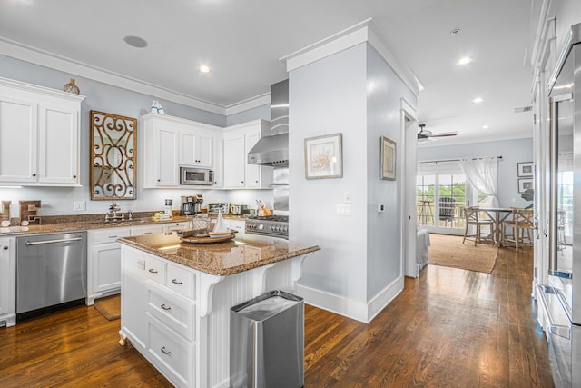 kitchen featuring stainless steel appliances, crown molding, stone counters, a ceiling fan, and wall chimney range hood